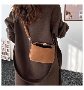 Close-up of caramel suede crossbody bag with gold buckle on a model in a brown coat