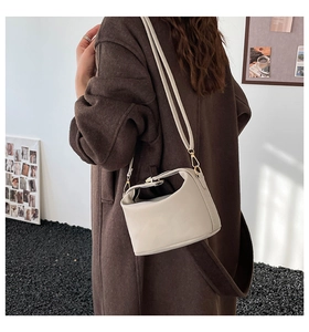 Close-up of a minimalist cream shoulder bag with gold hardware worn over a brown coat
