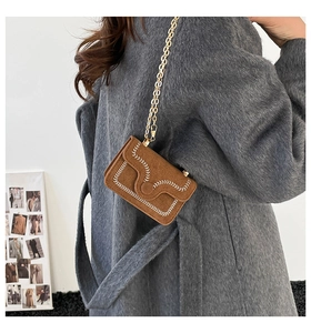 Brown suede crossbody bag with wavy stitching and gold chain on gray wool coat
