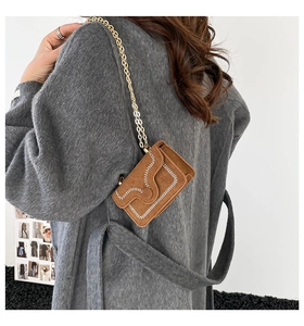 Detail of a brown suede mini card bag featuring white contrast stitching and a gold chain