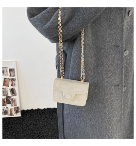 Detail of light beige crossbody bag with wavy stitching and gold chain on gray coat