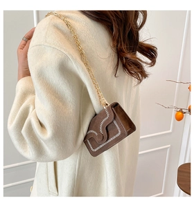 Close-up of brown suede mini crossbody bag with white stitching and gold chain strap