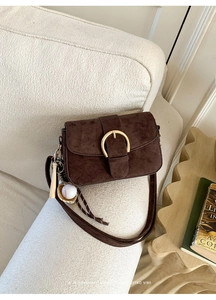 Detail of dark brown suede shoulder bag with gold metal buckle and baseball charm
