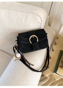 Close-up of black suede crossbody bag with gold round buckle and retro baseball charm