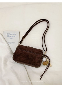 Detail of dark brown suede shoulder bag with creative baseball charm on white fabric