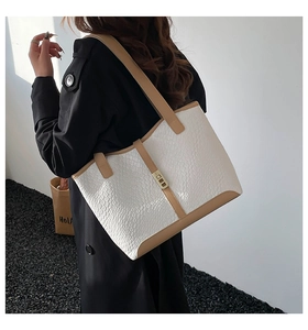 Detail of white woven tote bag with brown straps and gold lock on model in black coat
