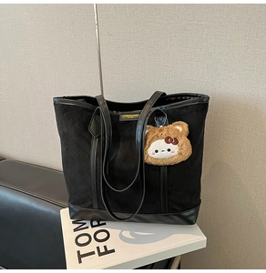 Detail of black tote bag with matte texture and cute brown plush bear charm accessory