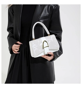 Détail du sac à main en cuir blanc avec fermoir doré et motif de lettres sur costume noir