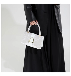 Detailed close-up of white crossbody bag featuring golden D-shaped buckle and letter print