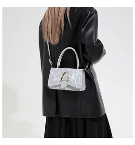 Detail of light gray square bag with gold triangular lock on black leather coat