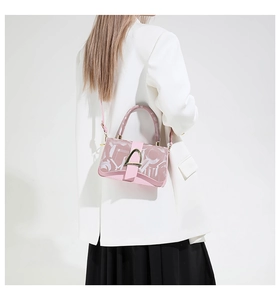Pink minimalist crossbody bag with metal horseshoe buckle worn by a model in a white suit