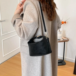 Chic black matte leather bucket bag with gold clasp shown on a model for scale and style