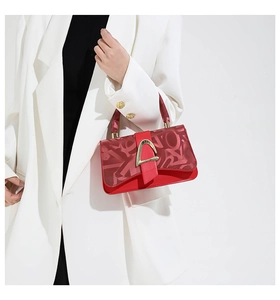 Détail du sac rouge avec fermoir doré et foulard imprimé enroulé sur la poignée