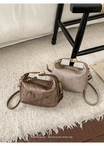 Close-up of minimalist textured leather Boston bags with gold hardware on a plush white rug