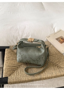 Detail of green crossbody bag with gold hardware on a textured woven stool