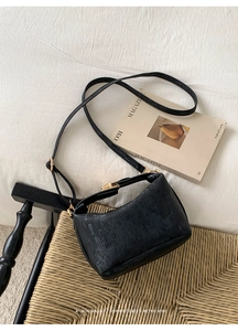Close-up of minimalist black handbag with vertical stripe texture and gold hardware on a chair
