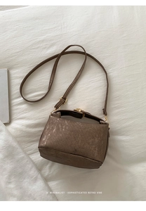 Detailed close-up of brown textured crossbody bag with a gold metal push-lock buckle