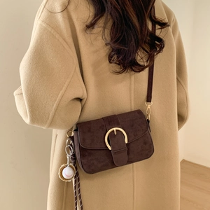 Brown suede crossbody bag with gold buckle and baseball charm over camel wool coat