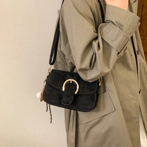 Classic black suede shoulder bag with gold buckle on a model in a khaki trench coat