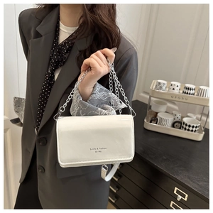Close-up of glossy white patent leather shoulder bag with silver chain and logo