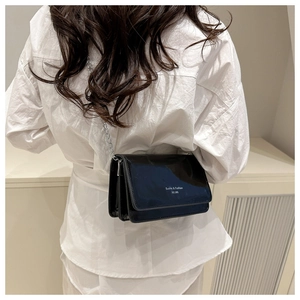 Detailed view of the shiny black patent leather crossbody bag with silver chain strap