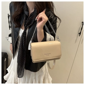 Close-up of beige patent leather bag with chain strap and Sunlta fashion logo print