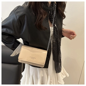 Close-up of cream glossy chain bag with flap design worn by a model in black leather jacket