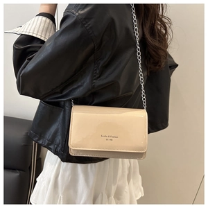 Close-up of beige patent leather shoulder bag with silver chain worn over a black leather jacket