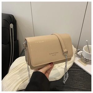 Detail of beige patent leather flap bag with silver chain strap and logo lettering