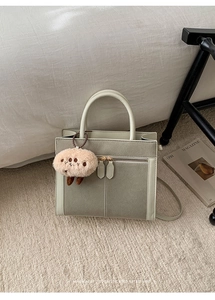 Détail d'un cabas en daim vert clair et gris avec pendentif en peluche sur tapis doux