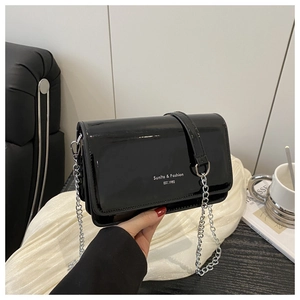 Macro view of black glossy leather flap bag with silver chain strap and white text