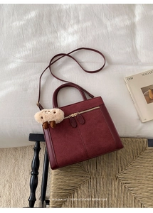 Detailed view of vintage burgundy matte shoulder bag with dual zippers and plush charm