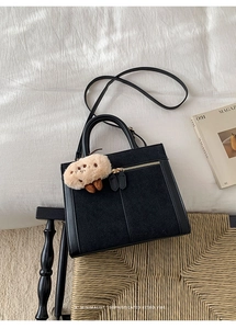 Detailed view of a black retro bag featuring leather patchwork and a cute plush charm
