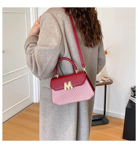 Detail van rood-wit gestreepte crossbodytas met gouden M-gesp gedragen door model