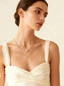 Detalle de collar de doble capa dorado con perla blanca y colgante de estrella en una modelo