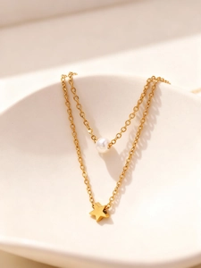 Primer plano de un collar doble dorado con perla y colgante de estrella en bandeja de cerámica