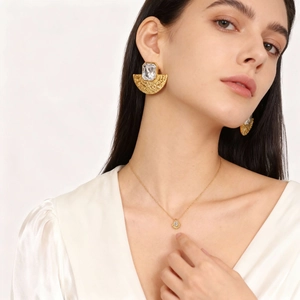 Détail de boucles d'oreilles dorées en éventail avec cristal et collier à pendentif