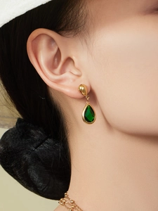 Detalle de pendientes de gota dorados con cristal verde en forma de pera sobre modelo