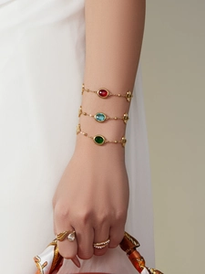 Detalle de tres pulseras doradas con piedras ovaladas rojas, azules y verdes y tréboles