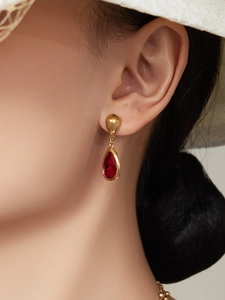 Detalle de pendiente de gota chapado en oro con cristal rojo en una modelo elegante