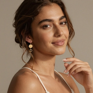 Boucle d'oreille en acier inoxydable doré avec pendentif lettre D portée par un mannequin