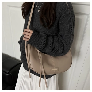 Detail of apricot crescent bag featuring golden hardware logo and long fringe tassels