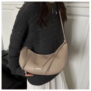 Detail view of a minimalist beige crescent bag with smooth leather and metal emblem