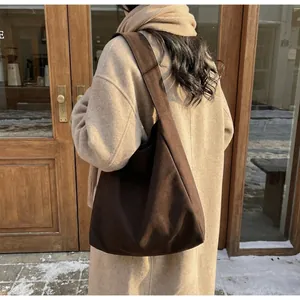 Dettaglio della borsa tote in pelle scamosciata marrone scuro con tracolla larga sul modello
