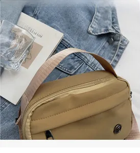 Détail du sac bandoulière en nylon kaki montrant la fermeture éclair et le logo
