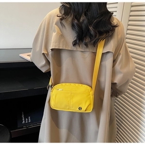 Detailed back view of a yellow nylon crossbody bag worn over a beige trench coat