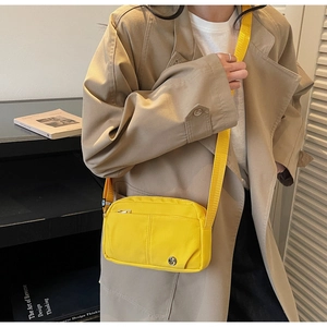 Gros plan d'un sac bandoulière en nylon jaune vif avec large sangle sur un trench-coat kaki