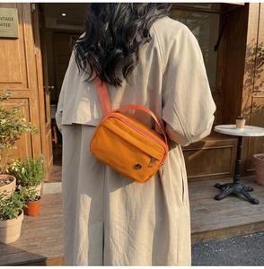Sac bandoulière en nylon orange vif porté avec un trench beige lors d'un shooting de rue