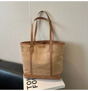 Detail of earthy brown tote bag in matte suede with glossy leather trim and golden logo