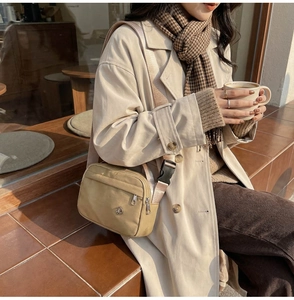 Sac bandoulière en nylon kaki avec double fermeture éclair porté avec un trench-coat chic